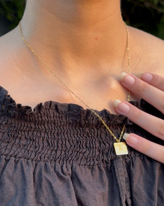 Gold necklace with a square pendant worn by a person against a dark background